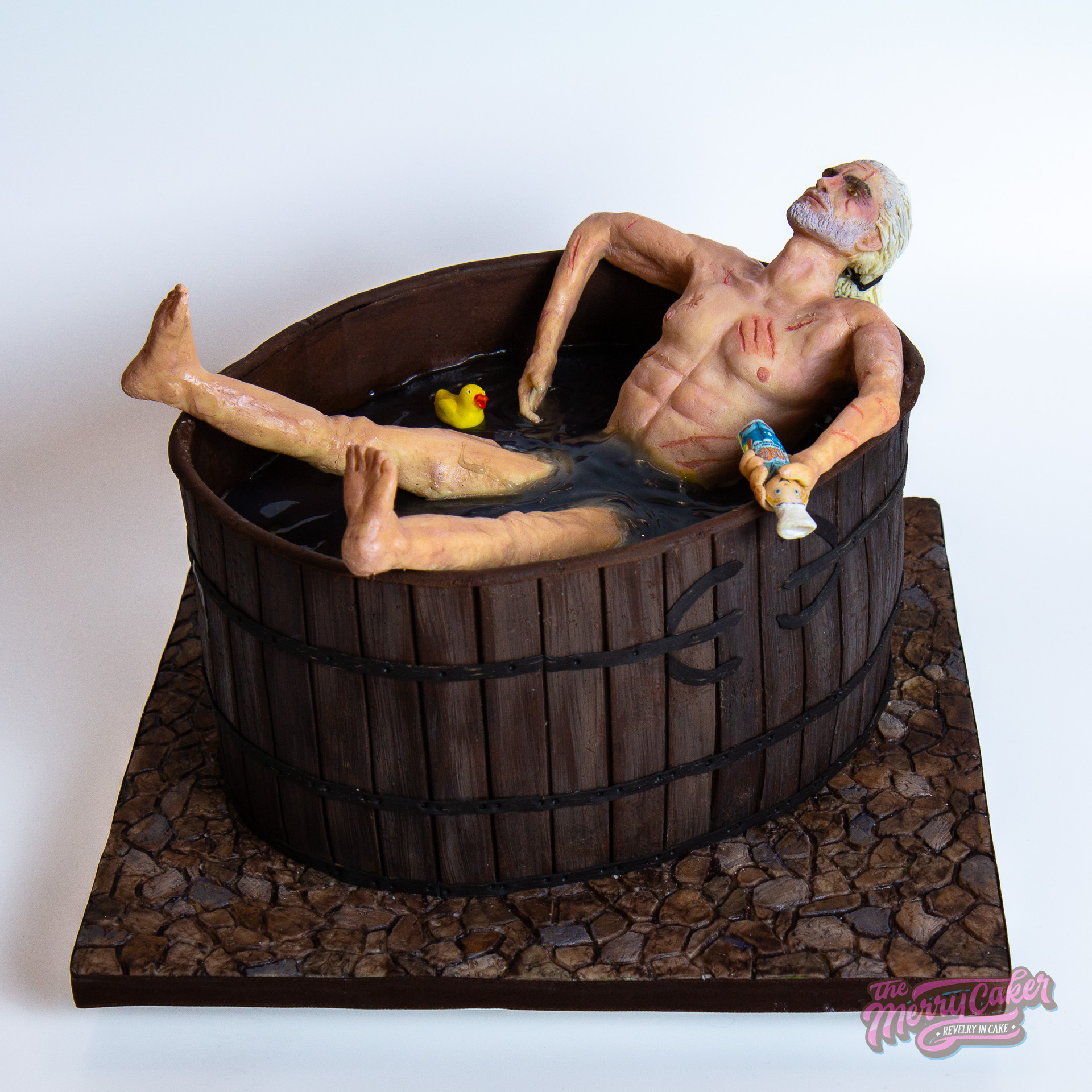 A realistic cake version of Geralt in the bathtub from the game and TV series The Witcher. Geralt is lying in the bathtub with a bottle of Matey bubblebath in his hand and there is a rubber duck next to him in the water.