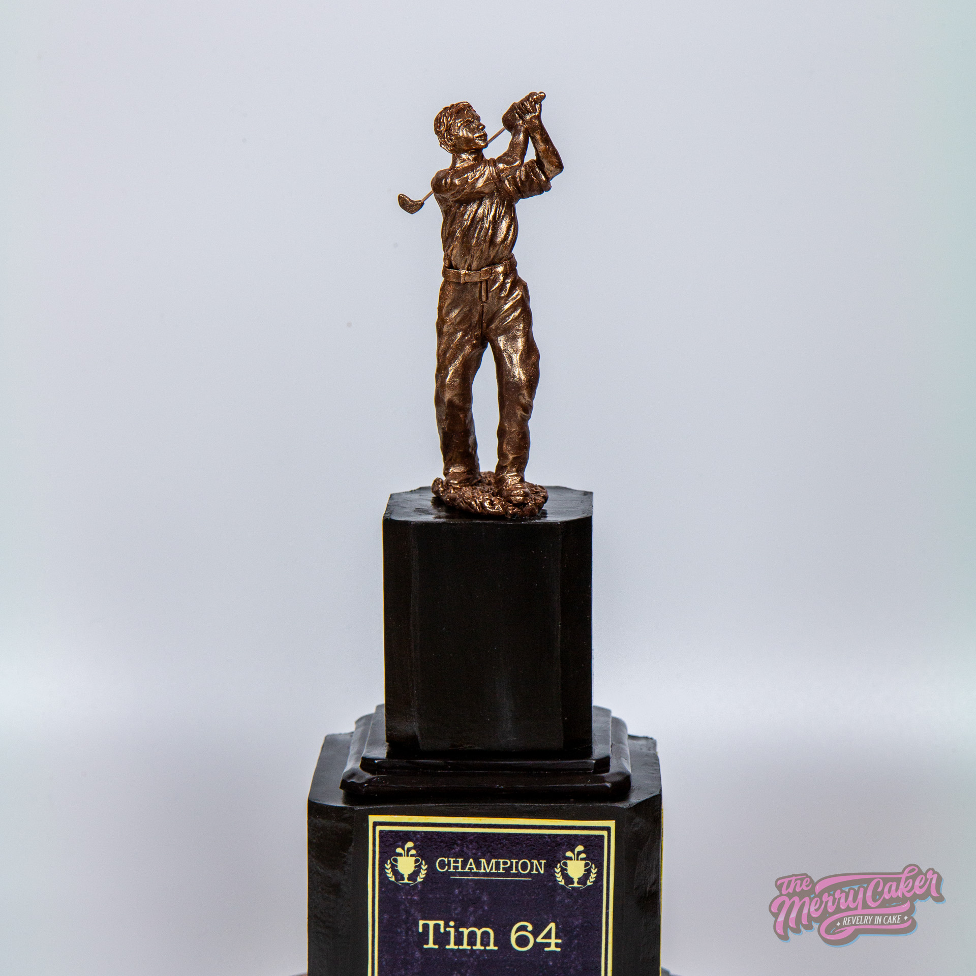 A realistic two tier black golf trophy cake with a bronze chocolate golfer statue on the top
