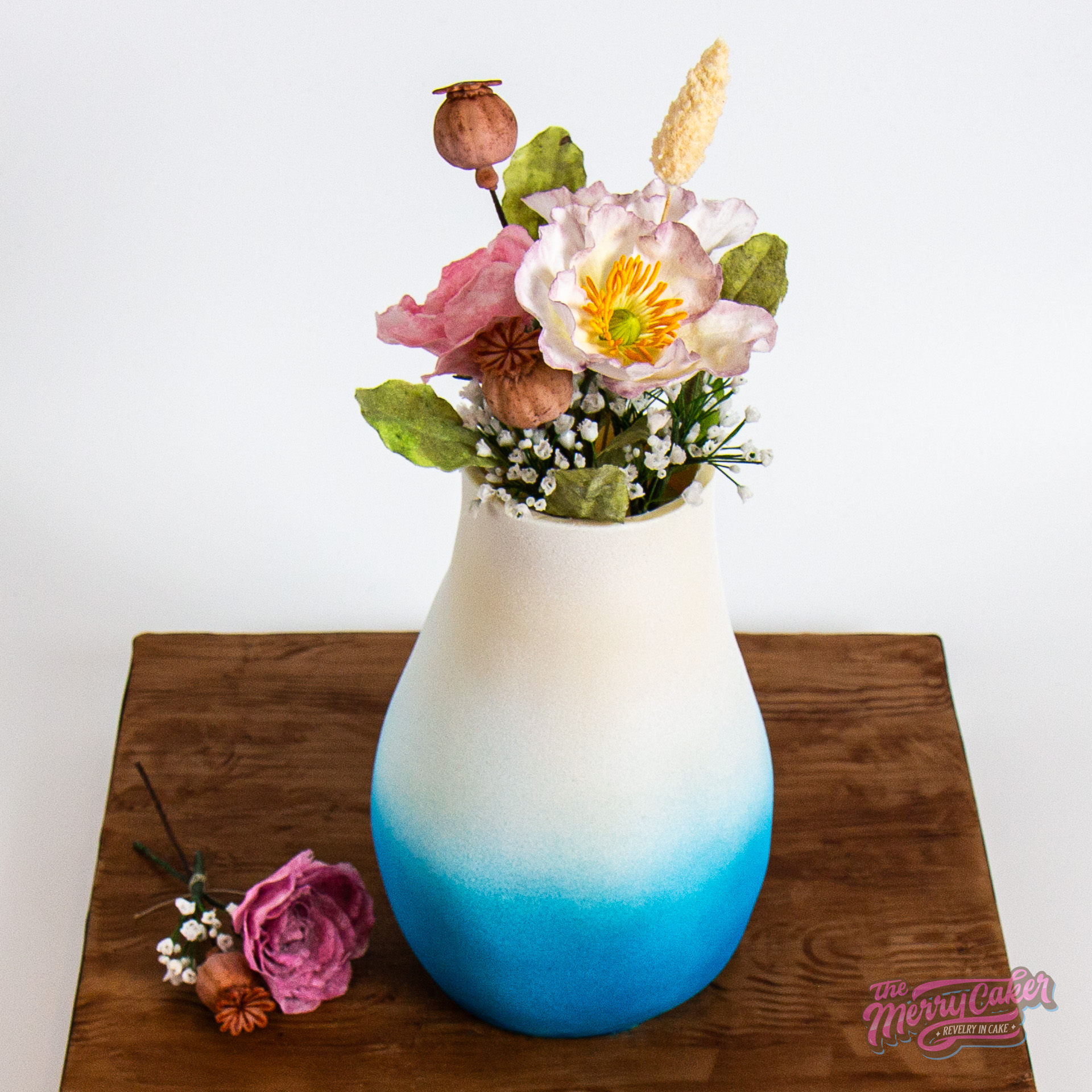A realistic blue and white vase cake with a bouquet of wafer paper and sugarpaste flowers coming out of the top